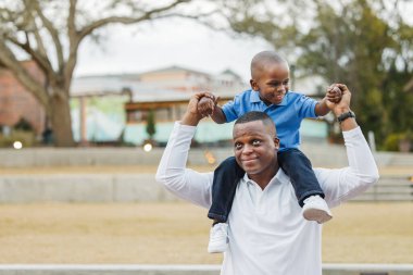 Anaokulundaki oğlunu omuzlarında taşıyan bir baba.