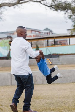 Bir baba, genç oğlunu bir uçak gibi sallıyor.