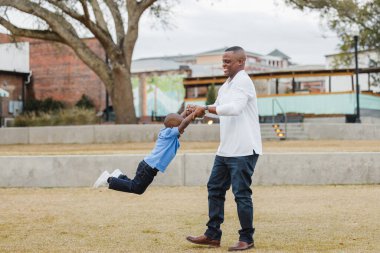 Bir baba, genç oğlunu bir uçak gibi sallıyor.