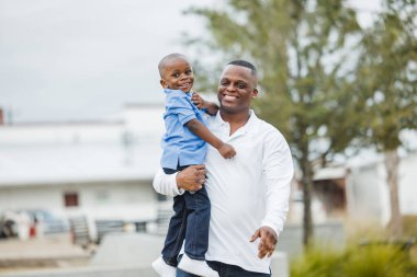 Genç bir çocuk ve babası dışarıda kameraya bakıyor.