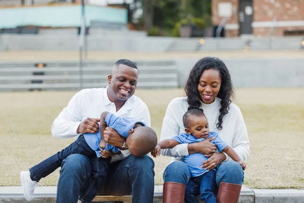 Красивые афроамериканские мама и папа сидят на ступеньках и щекочут своих сыновей, и все смеются. — стоковое фото