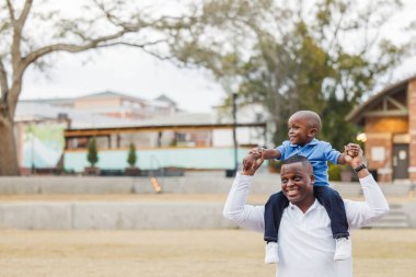 Anaokulundaki oğlunu omuzlarında taşıyan bir baba.