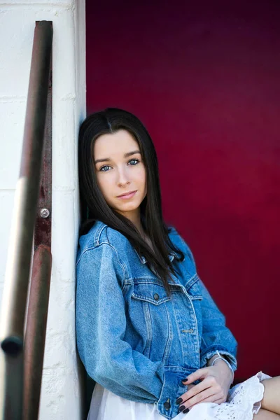 A beautiful teen brunette girl with a serious look leaning against a wall in thought with a pink red background — Stock Photo, Image