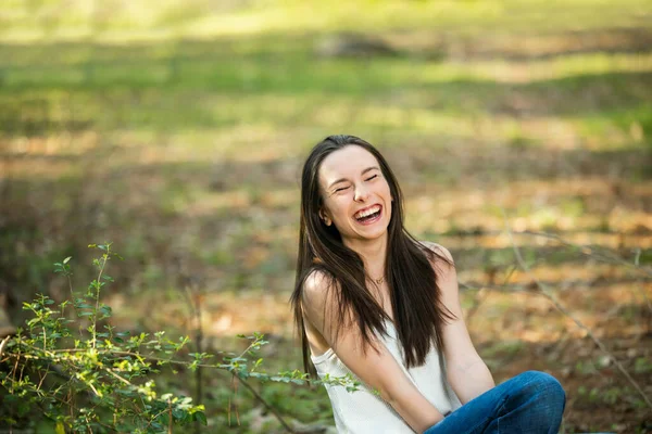 Krásná šťastná dospívající brunetka dívka sedí venku a nekontrolovatelně se směje něčemu legračnímu — Stock fotografie