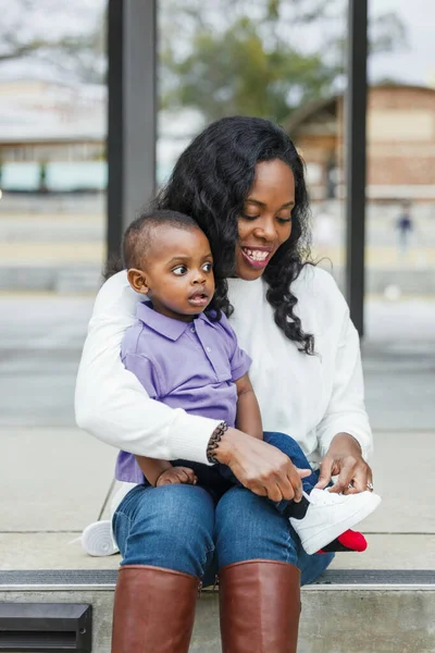 Красивая афро-американская мама, сидящая на ступеньках и завязывающая кроссовки своим маленьким сыновьям — стоковое фото