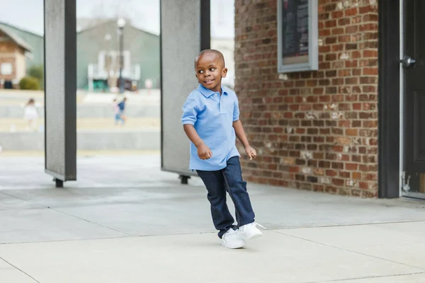 A cute little boy of preschool age with a blue shirt downtown in the city wearing denim jeans running around — стоковое фото