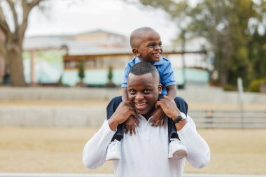 Anaokulundaki oğlunu omuzlarında taşıyan bir baba.