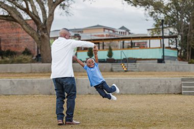 Bir baba, genç oğlunu bir uçak gibi sallıyor.