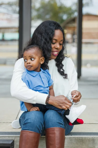 Красивая афро-американская мама сидит на ступеньках на улице и завязывает кроссовки своим маленьким сыновьям — стоковое фото