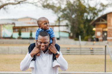 Anaokulundaki oğlunu omuzlarında taşıyan bir baba.