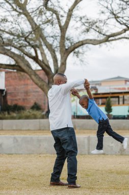 Bir baba, genç oğlunu bir uçak gibi sallıyor.