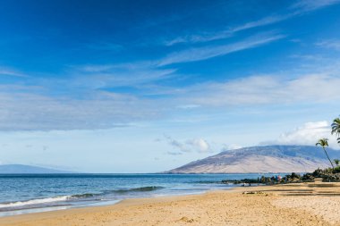 Maui Hawaii 'de kumlu, dalgalı ve uzak bir dağlı bir sahil..