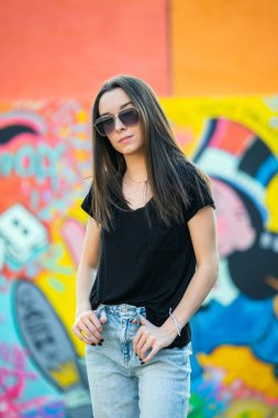 Havacı güneş gözlüklü, çok renkli bir duvara yaslanmış güzel, ciddi bir genç kız..