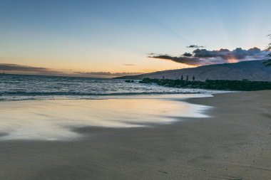 Maui Hawaii beach coastline of sand, sun, and blue water with crashing at sunset.