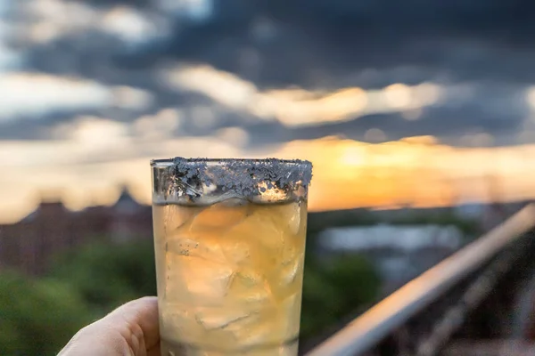A classic margarita at a rooftop bar in Savannah, Georgia at sunset with a railing and moody sky in view.