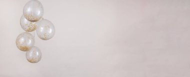 A monochromatic gold, off white and beige confetti clear balloons against a light beige backdrop for a banner with copy space.
