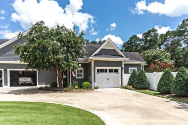 Low angle view of the side of a large gray craftsman new construction house with a landscaped yard a an open garage.