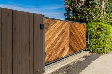 Stained natural wood modern and clean wood driveway property private gate entrance in a tropical location with secure gate access pinpad.