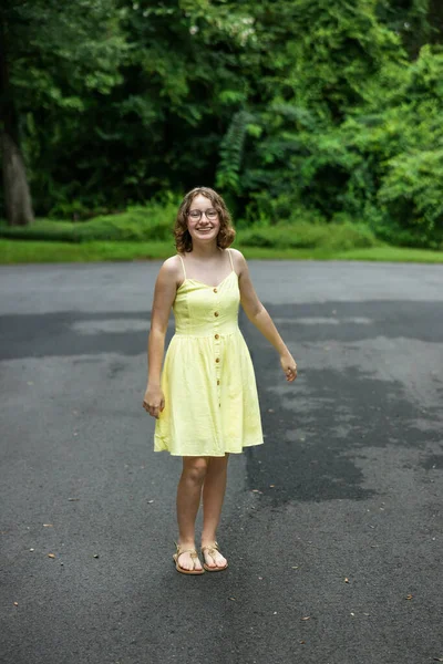 Tween almost teenage girl with braces and wearing a yellow sundress outside in the summer.