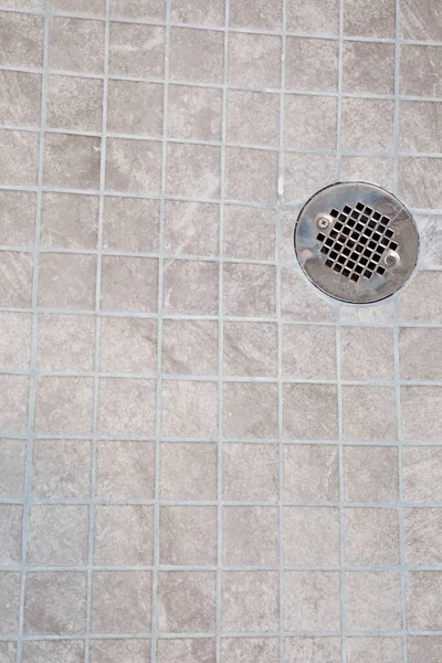 A neutral light beige square tile shower floor with a silver metal drain.