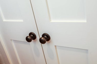 A set of double white wood interior doors with dark black or oil rubbed broze doorknobs for a closet or room door opening.