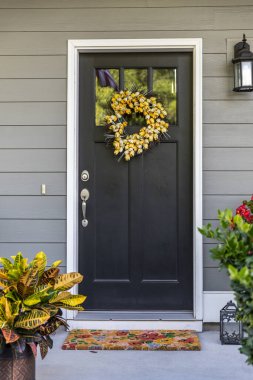 A black front door to a townhouse, apartment or condominium with a yellow wreath.