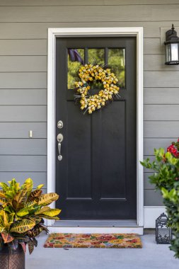 A black front door to a townhouse, apartment or condominium with a yellow wreath. clipart