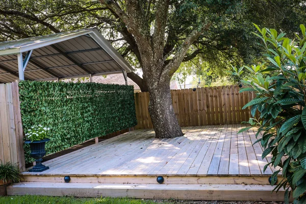 A small built out pressure treated wood deck space built around a tree with a greenery covered wall to the garage.