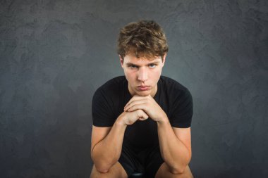 An angry young man sitting and leaning forward on his knees angry, mad and upset with a threatening look.