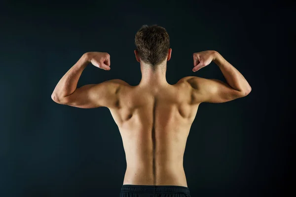 A man making muscles with his arms from behind showing a muscular and fit back on a black background.