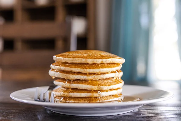 A plate with a stack of plain homemade pancakes at a dark wood kitchen dining room table.