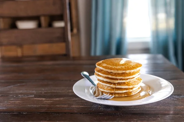 A plate with a stack of plain homemade pancakes at a dark wood kitchen dining room table.