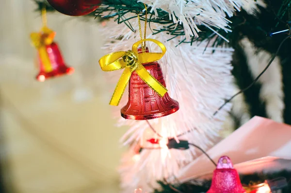 red little bell with yellow ribbon hanging on Christmas branch tree with blurred background, Christmas tree decoration