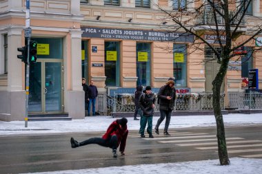 Riga, Letonya: 17 Ocak 2022: Kadın kış aylarında kaygan ve buzlu bir caddeye düşer. Sokakta kayıp düşen kız. Seçici odak
