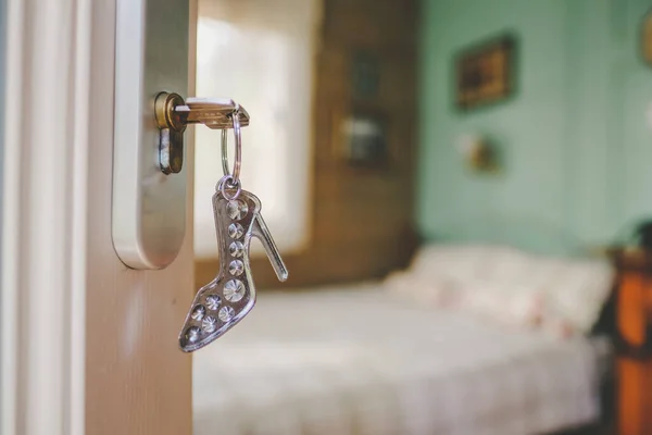 Hotel room and keys in the door with a keychain - a stylized womans high-heeled shoe. Prostitution, extramarital affairs. Defocused. High quality photo
