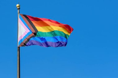 Bir LGBTQ + gökkuşağı gelişimi bir bayrak direğinden dalgalanan gurur bayrağı. Arkadaki mavi gökyüzü.