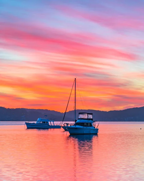 A colourful sunrise with boats, high cloud and reflections at Koolewong Waterfront on the Central Coast, NSW, Australia.