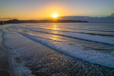 Denizin üzerinde gün doğumu Orta Sahildeki Umina Sahili 'nde dalgalarla, NSW, Avustralya.