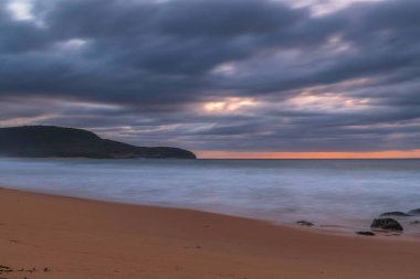 Kumsalda kayalarla birlikte gün doğumu denizi ve Orta Sahildeki Killcare Sahili 'nden gelen alçak bulutlar, NSW, Avustralya.