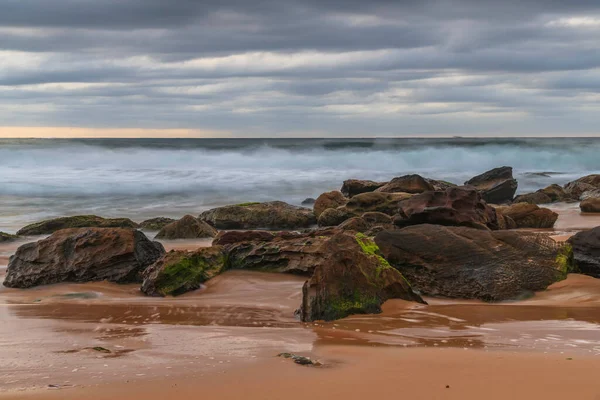 澳大利亚新南威尔士州中部海岸的日出海景 海滩上有岩石 低云密布 — 图库照片
