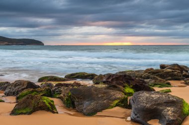 Kumsalda kayalarla birlikte gün doğumu denizi ve Orta Sahildeki Killcare Sahili 'nden gelen alçak bulutlar, NSW, Avustralya.