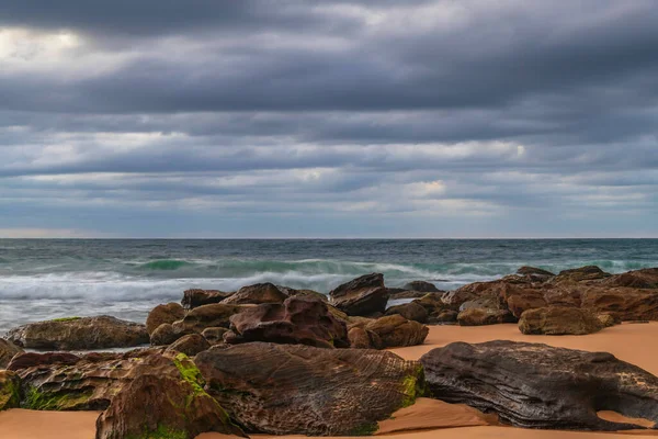 澳大利亚新南威尔士州中部海岸的日出海景 海滩上有岩石 低云密布 — 图库照片