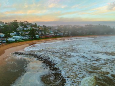 Merkezi Sahildeki Avoca Sahili, NSW, Avustralya 'da bulutlu, sisli ve deniz köpüklü gündoğumu denizi..