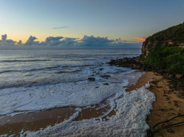 Gündoğumu deniz köpüğü ve sel enkazı ile birlikte Central Coast, NSW, Avustralya 'daki Killcare Sahili' nde..