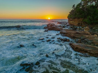 Central Coast, NSW, Avustralya 'daki Avoca Sahili' nde sörfçülerle ve kayalarla gün doğumu deniz manzarası.