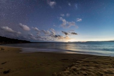 NSW, Avustralya 'nın merkez kıyısındaki Putty Plajı' nda yıldızlı bir gökyüzünün altında Palm Beach ve Sydney ışıkları uzakta parlıyor..