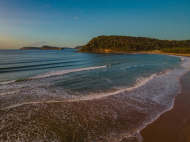 Güneş doğarken küçük dalgalar ve çoğunlukla açık gökyüzü ile Central Coast, NSW, Avustralya 'daki Umina Sahili' nde.
