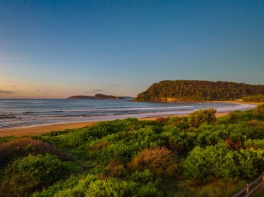 Güneş doğarken küçük dalgalar ve çoğunlukla açık gökyüzü ile Central Coast, NSW, Avustralya 'daki Umina Sahili' nde.
