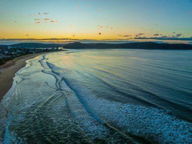 Güneş doğarken küçük dalgalar ve çoğunlukla açık gökyüzü ile Central Coast, NSW, Avustralya 'daki Umina Sahili' nde.