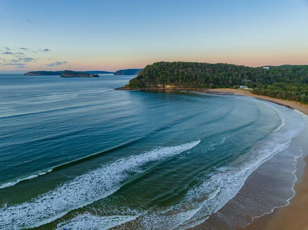 Güneş doğarken küçük dalgalar ve çoğunlukla açık gökyüzü ile Central Coast, NSW, Avustralya 'daki Umina Sahili' nde.